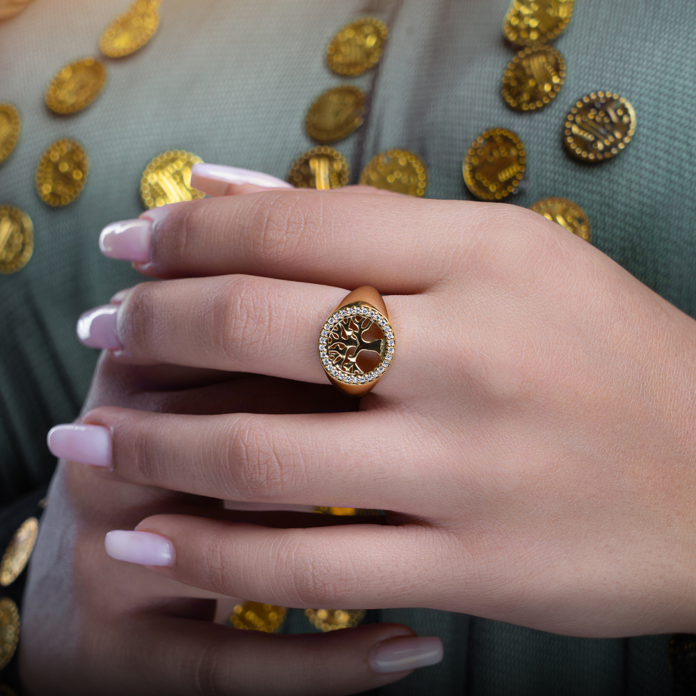 woman wearing a gold plated ring with a design featuring a tree and leaves, encrusted with cubic zirconia stones.