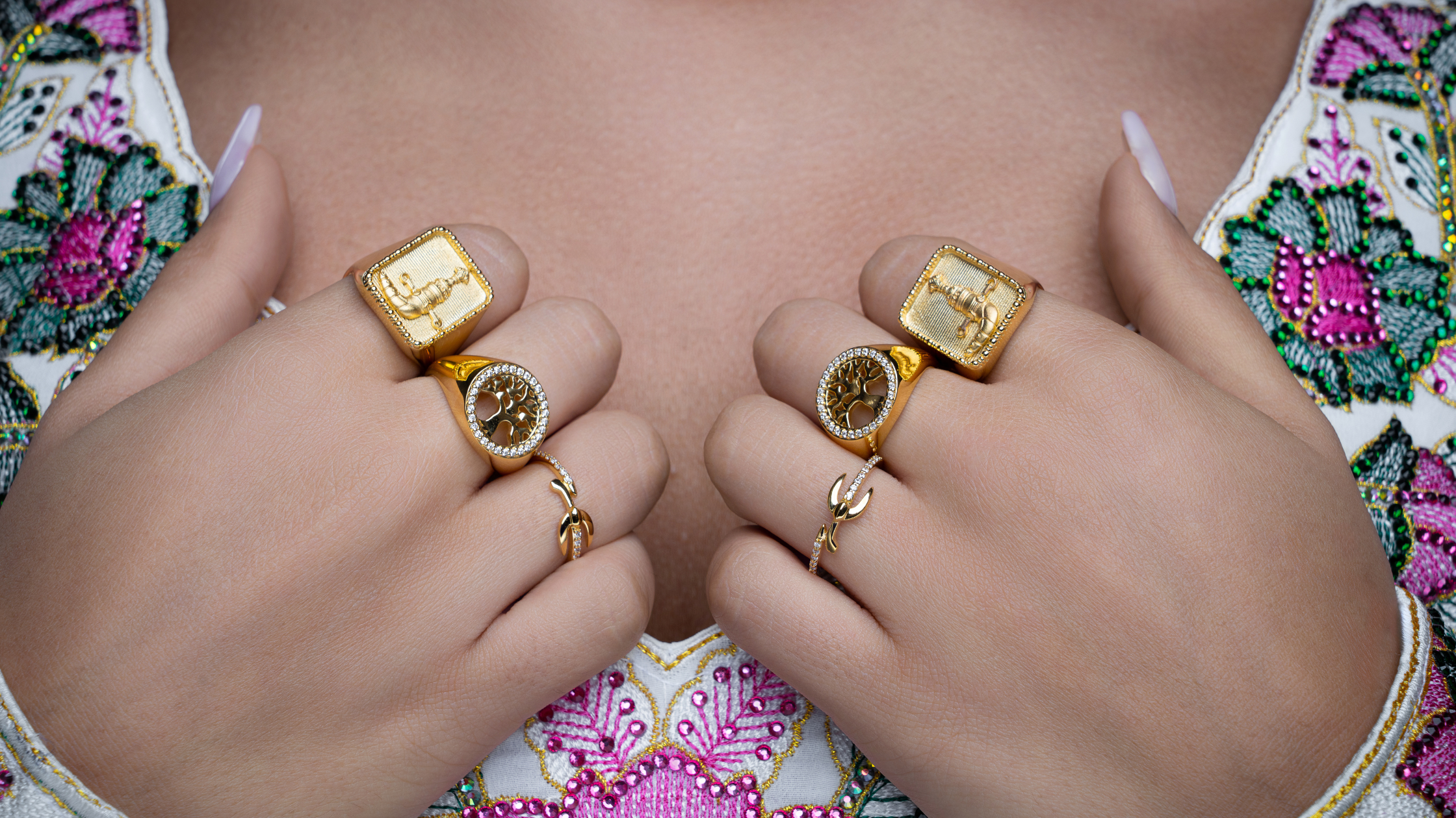 Close-up of hands wearing gold rings with a colorful embroidered garment in the background