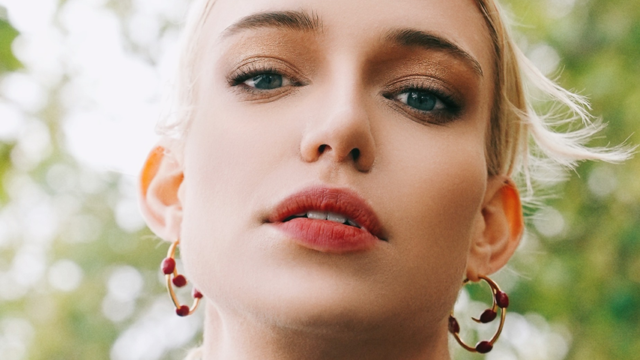 Close-up of a person with blonde hair and hoop earrings against a blurred green background