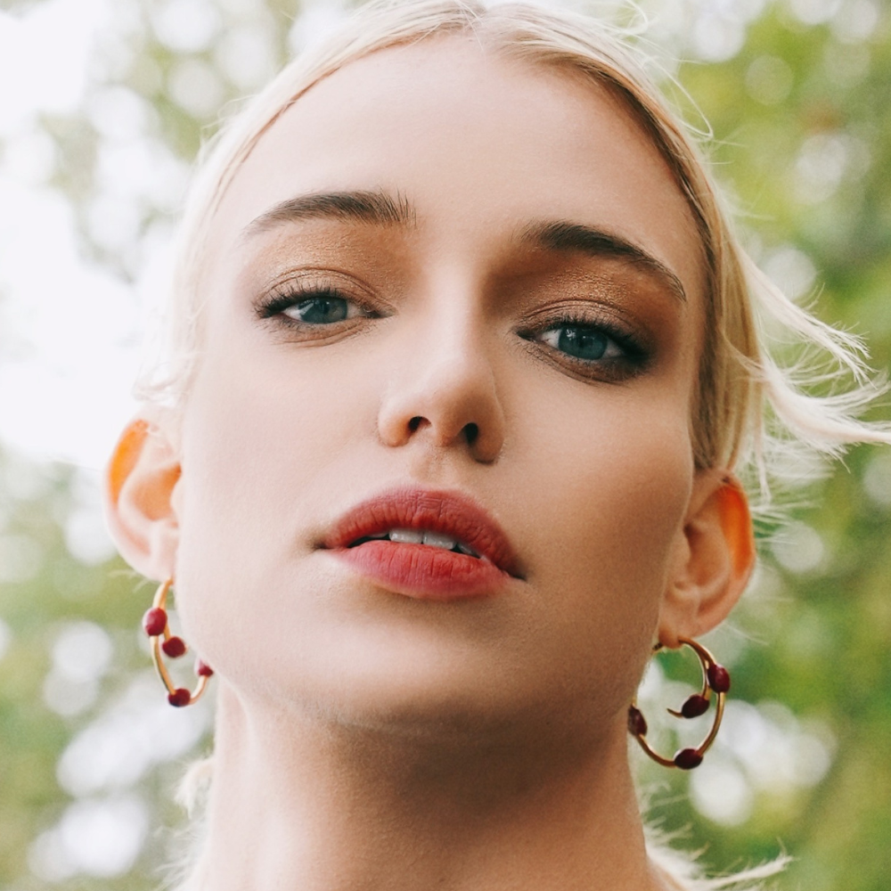 Woman wearing Athena gold-plated hoop earrings with maroon enamel