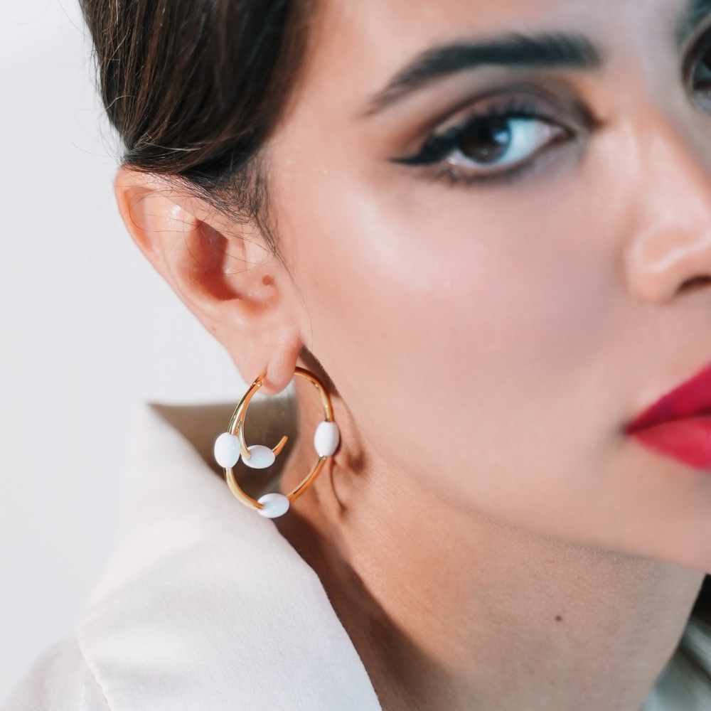 Woman wearing Athena gold-plated hoop earrings with white enamel finish