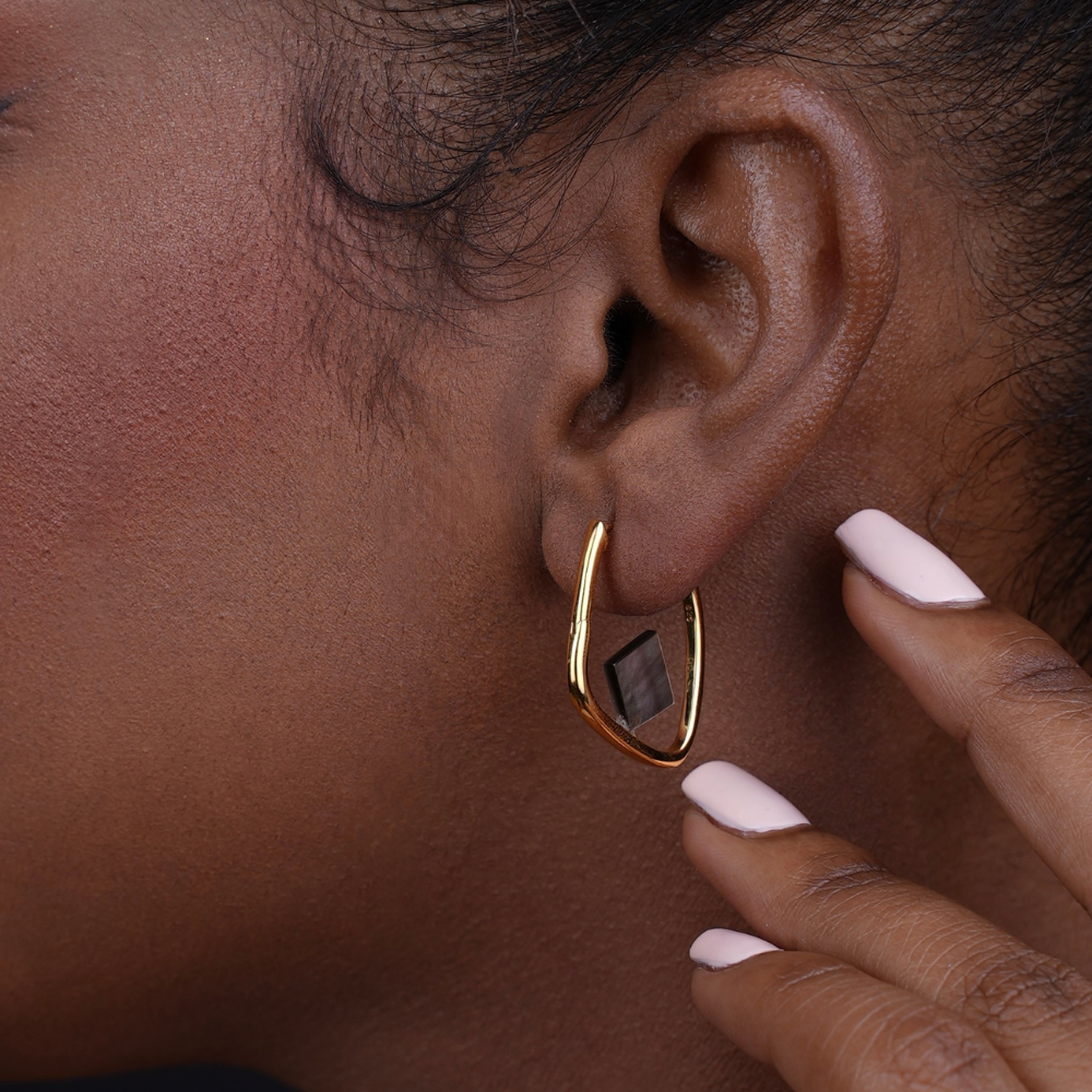 Woman wearing Aurora gold-plated hoop earrings with black mother-of-pearl accents