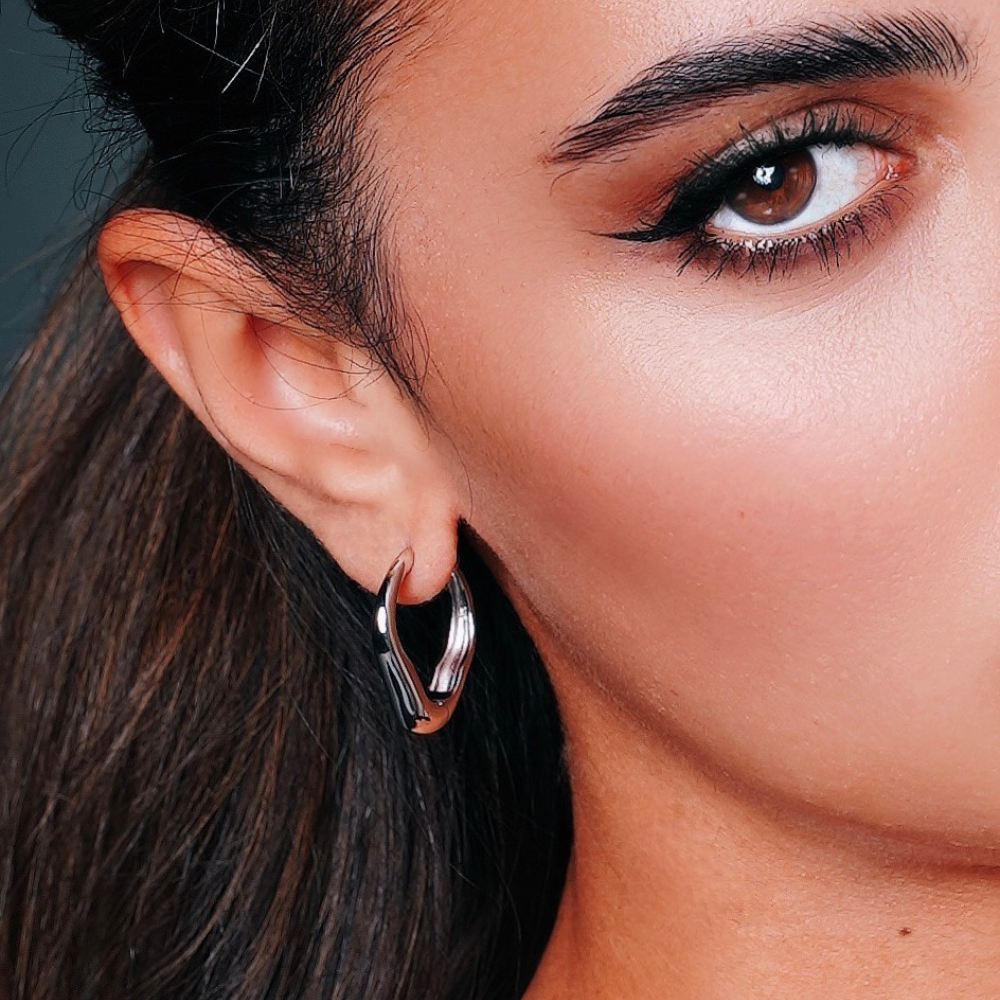Woman wearing sterling silver heart-shaped hoop earrings with minimal elegant design