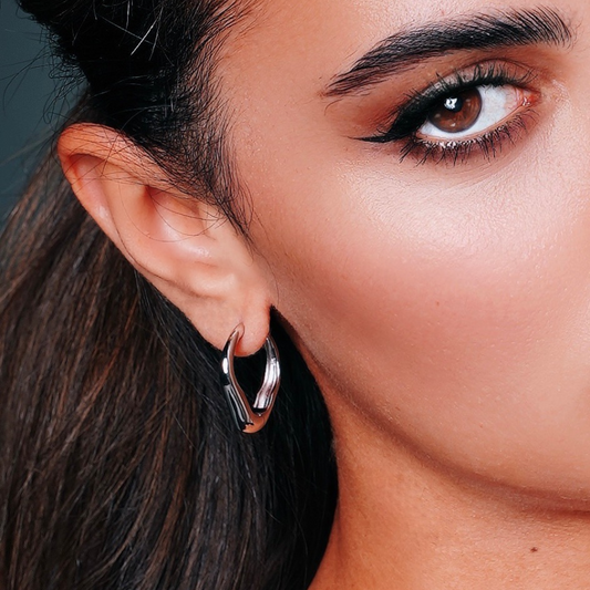Woman wearing sterling silver heart-shaped hoop earrings with minimal elegant design