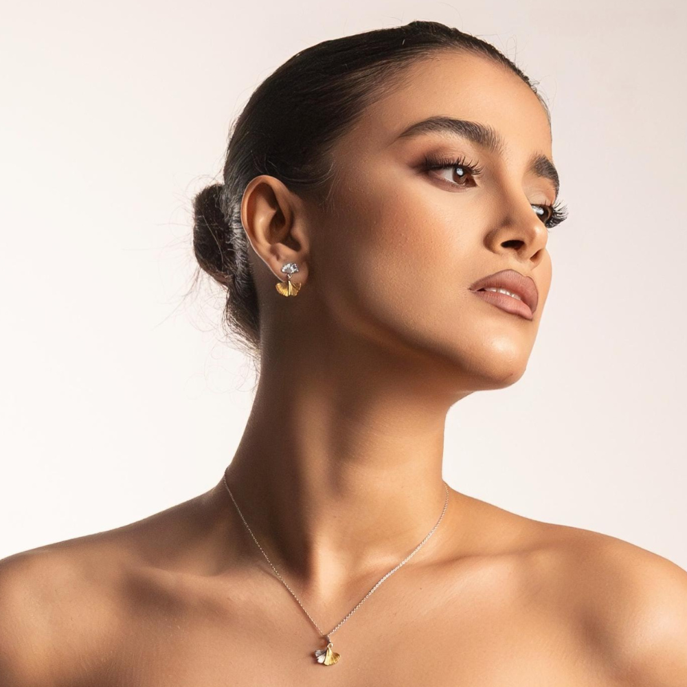 Woman wearing gold earrings and a necklace against a neutral background